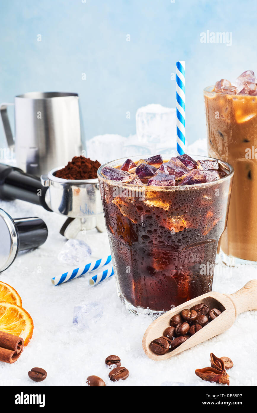 Summer drink iced coffee or soda in a glass and ice coffee with cream in a tall glass surrounded by ice, coffee beans, portafilter, tamper, milk jug a Stock Photo