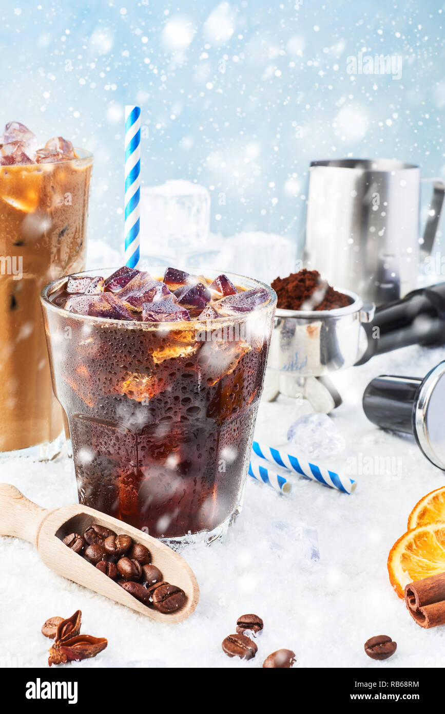 Winter drink iced coffee in a glass and ice coffee with cream in a tall glass surrounded by ice, coffee beans, portafilter, tamper, milk jug and vario Stock Photo