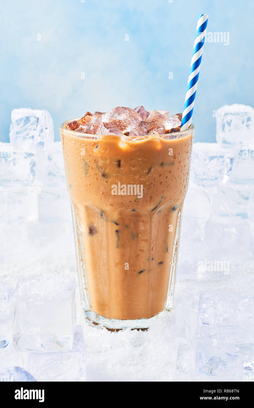 Summer drink ice coffee with cream in a tall glass with droplets and straw surrounded by ice cubes on snow over blue background. Selective focus, copy Stock Photo