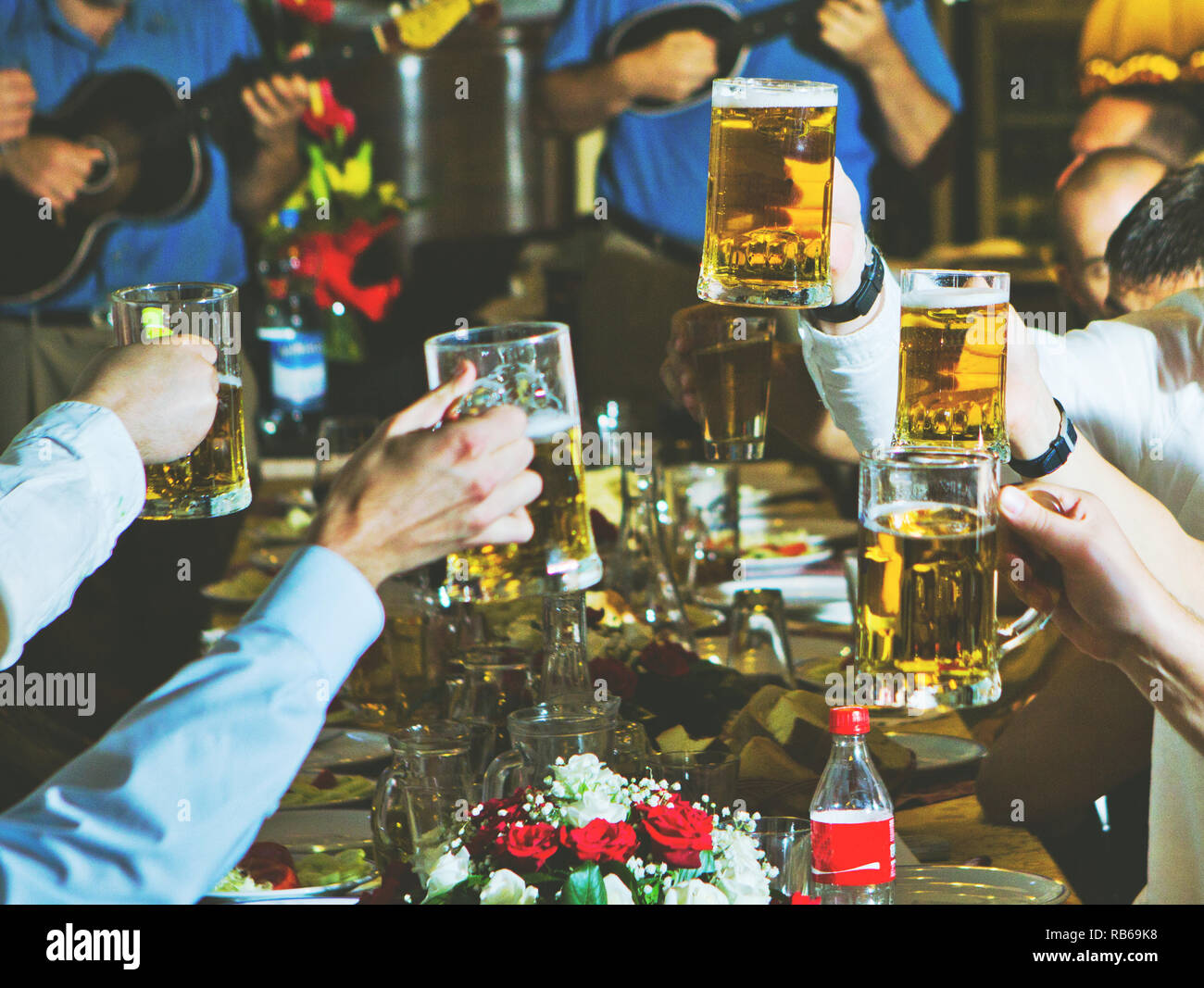 Friends toasting and cheering with beer at restaurant - Unrecognizable group of young people- Hands in focus - Cheers Stock Photo