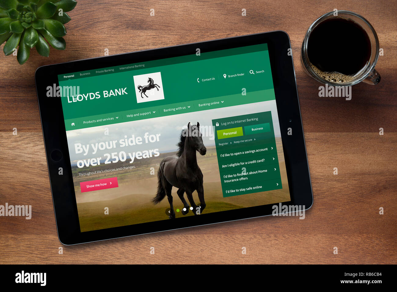 The website of Lloyds Bank is seen on an iPad tablet, on a wooden table along with an espresso coffee and a house plant (Editorial use only). Stock Photo