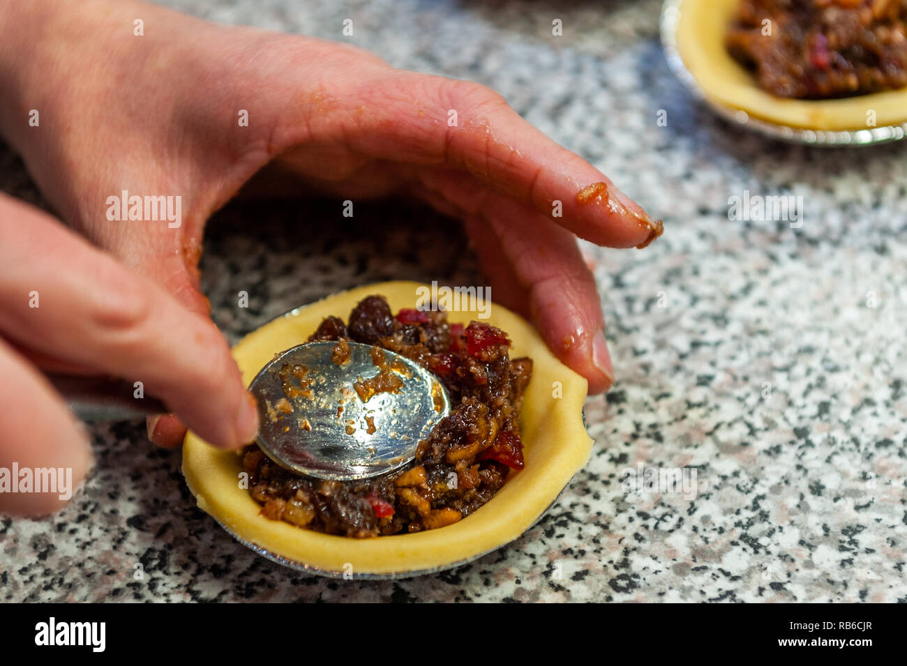 Woman baker putting mincemeat into a Christmas mince pie in a domestic kitchen. Stock Photo