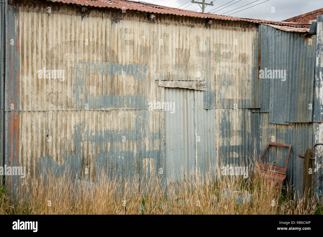 An old corrugated wall with old and weathered text with tall grass and an old car door in the foreground Stock Photo