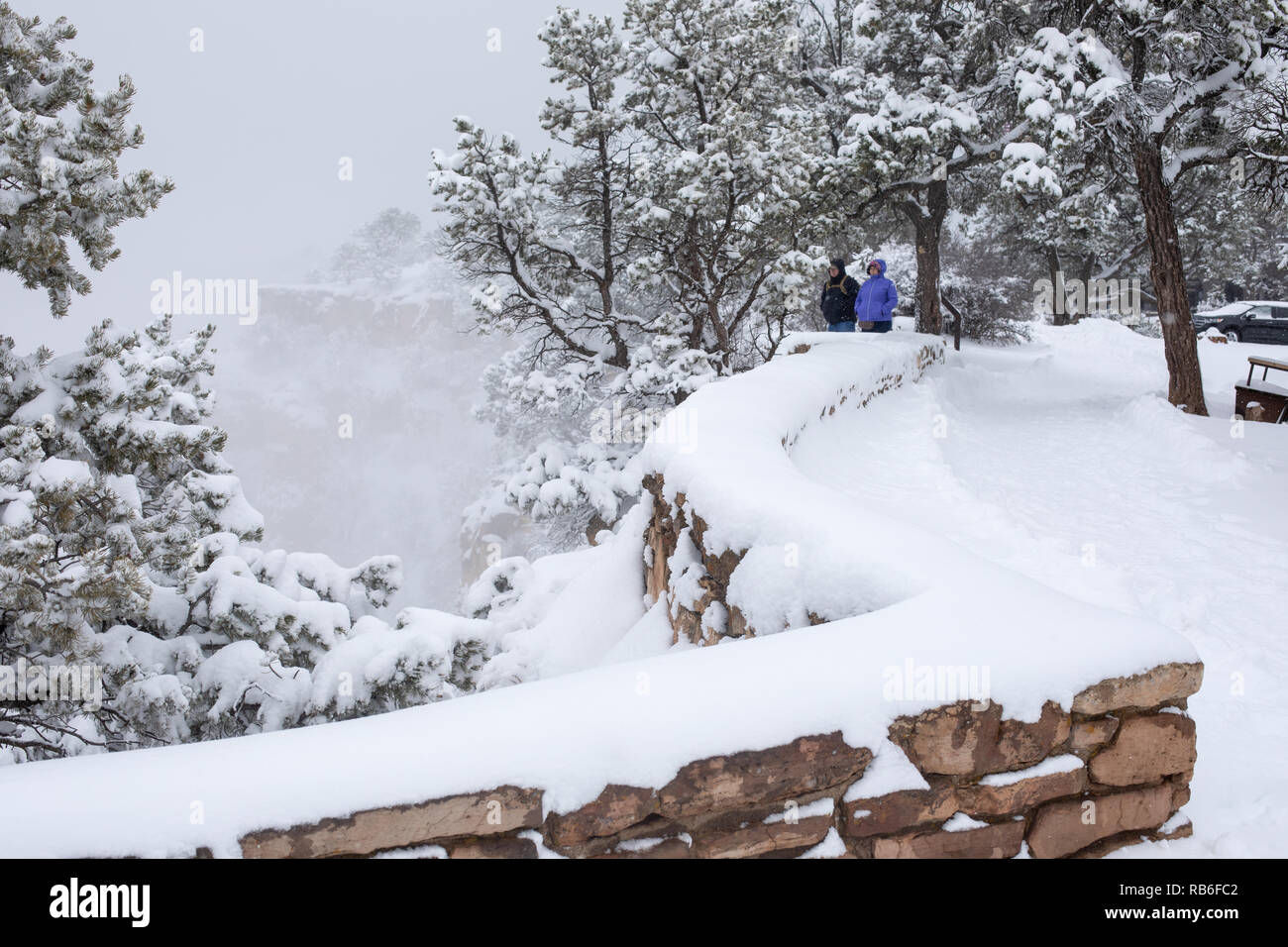 A couple looks out over a winter snow storm the Grand Canyon from the Rim Trail in Grand Canyon Village, USA Stock Photo