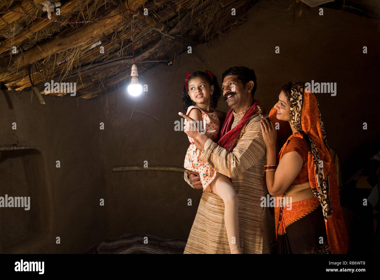 Rural Indian family delighted at the glow of light bulb and electricity reaching their home after long wait Stock Photo