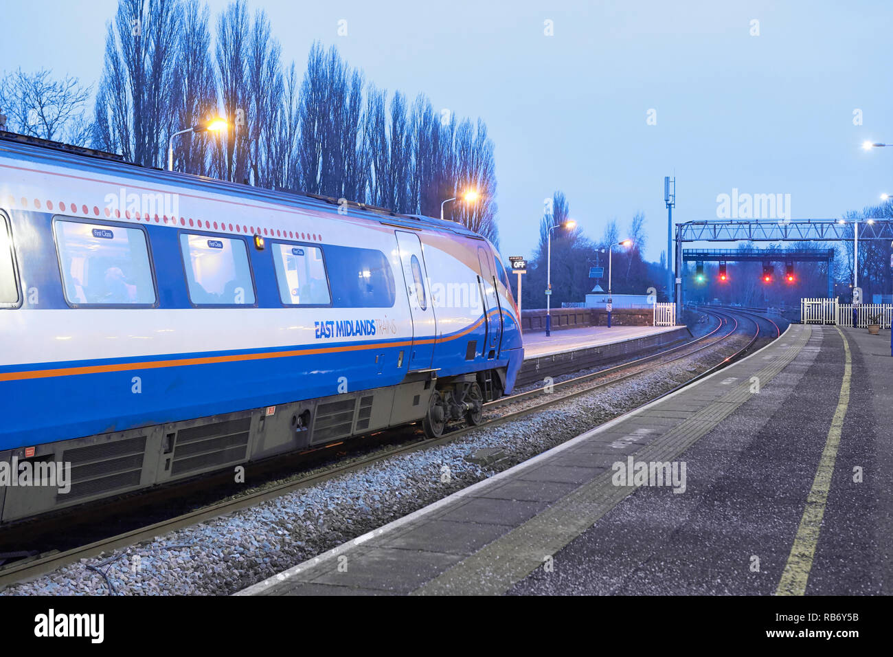 An East Midlands train and engine on the rail line beside the platform of the railway station at Kettering, England, as dawn breaks on a winter day. Stock Photo