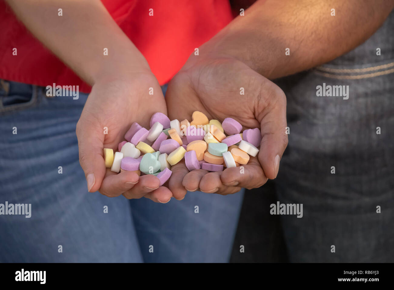 They hold each other close so not to drop any of the colorful heart shape Valentines Day candy. Stock Photo