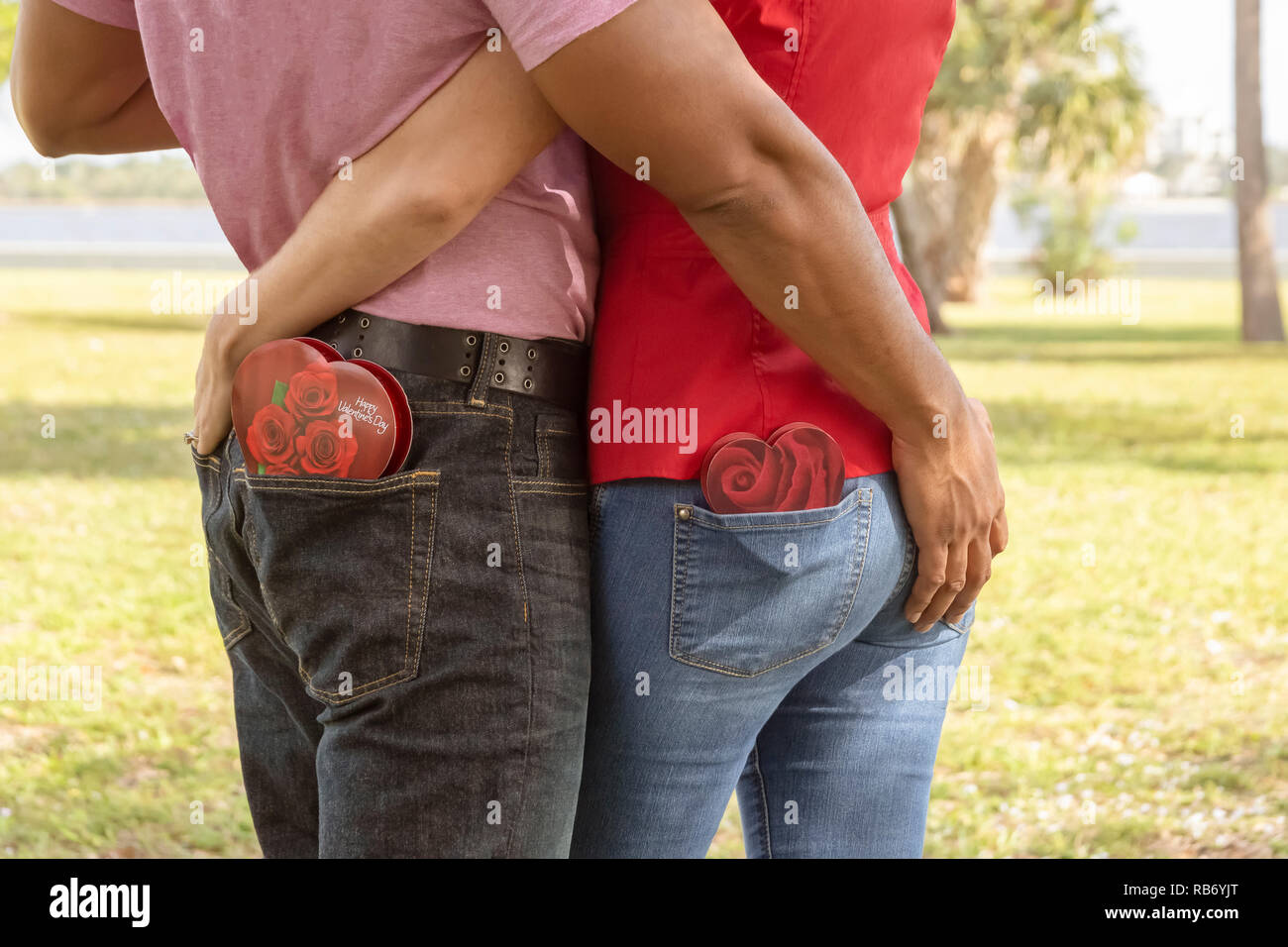 They hold each other's backside with chocolate hearts boxed candy in the opposite pocket. Stock Photo