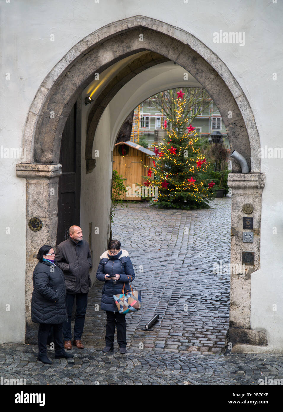 Thre people waiting in the medieval arched entrance to the Bischofshof Hotel in Regensburg. A Christmas tree can be seen in the courtyard beyond. Stock Photo