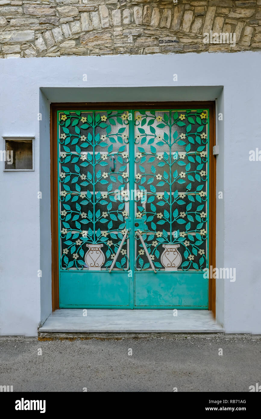 Traditioanl metal patterned doors in Cyprus village.  Aqua coloured leaves with white flowers and white vases.  Matching pair of doors. Stock Photo