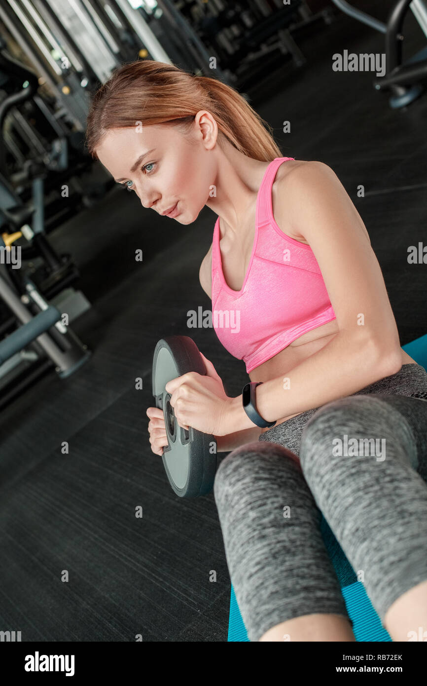 Young woman in gym healthy lifestyle sitting on yoga mat lifting plate ...