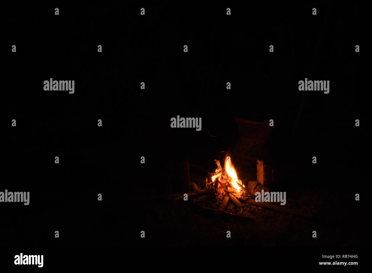 A bright camp fire with yellow and orange flames on a black dark ...