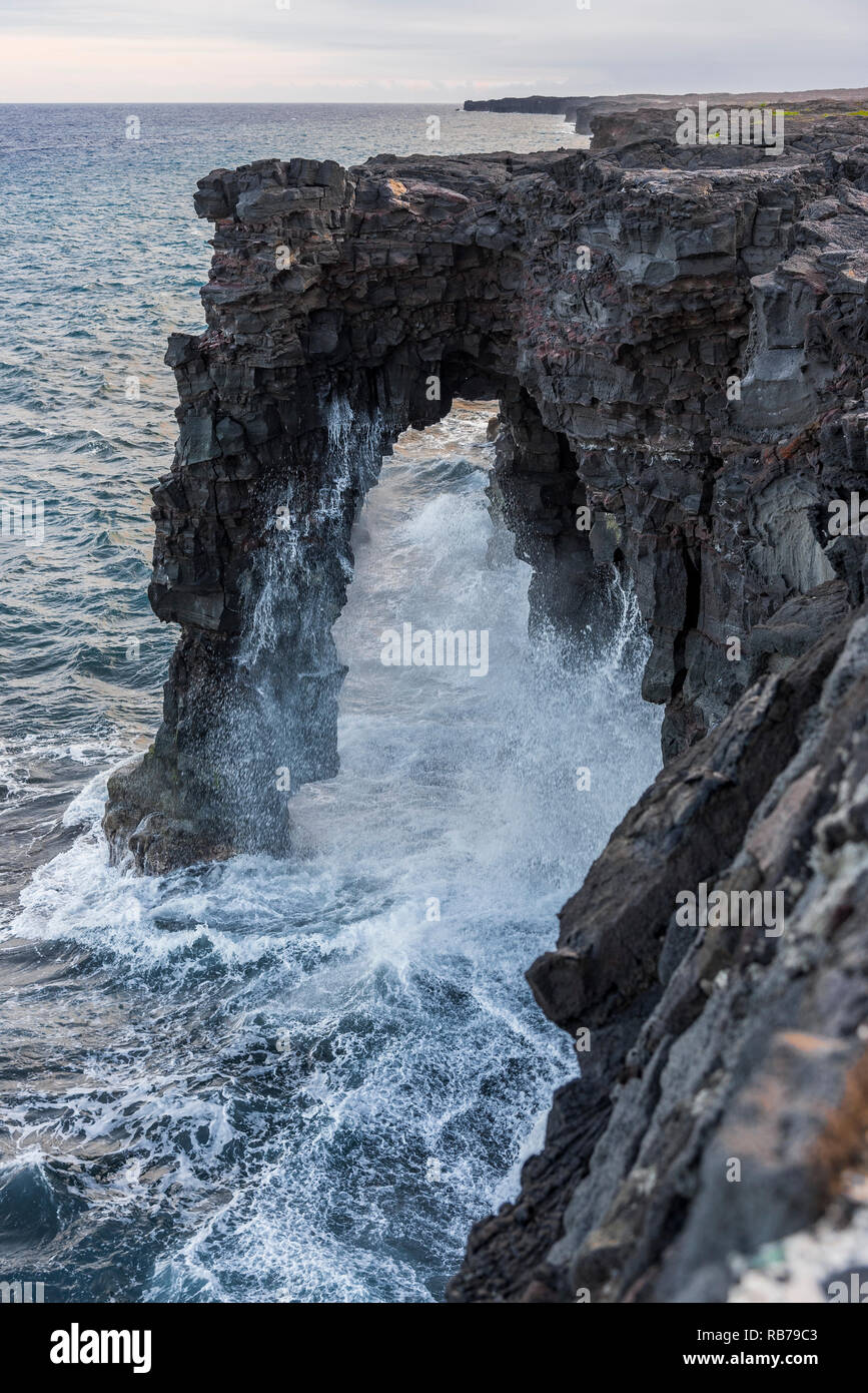 Waves crashing on a volcanic rock arch in Big Island, Hawaii Stock Photo