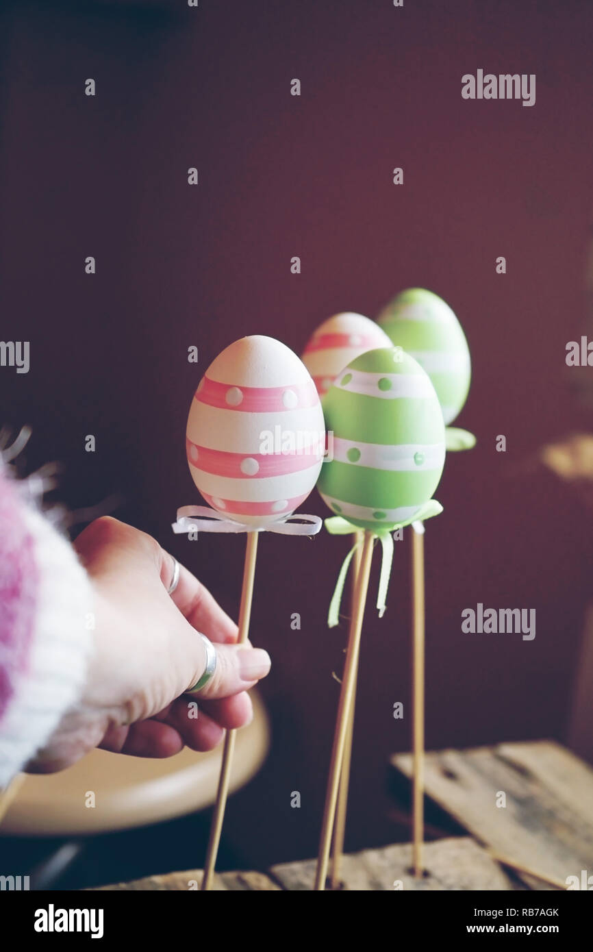 A beautiful close-up of 3 easter eggs on sticks over tables with a woman hand holding them and an amazing depth of field as background Stock Photo