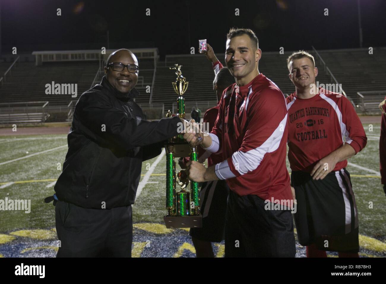 Joel Hines, left, director of the intramural sports program, Marine Corps Base Quantico (MCBQ), presents the first place trophy to the Base Motor Transport team during the Marine Corps Community Services Intramural Flag Football Championship Tournament at Butler Stadium, MCBQ, Va., Dec. 1, 2016. Marines from different units volunteer to compete in an intermural flag football league. Stock Photo