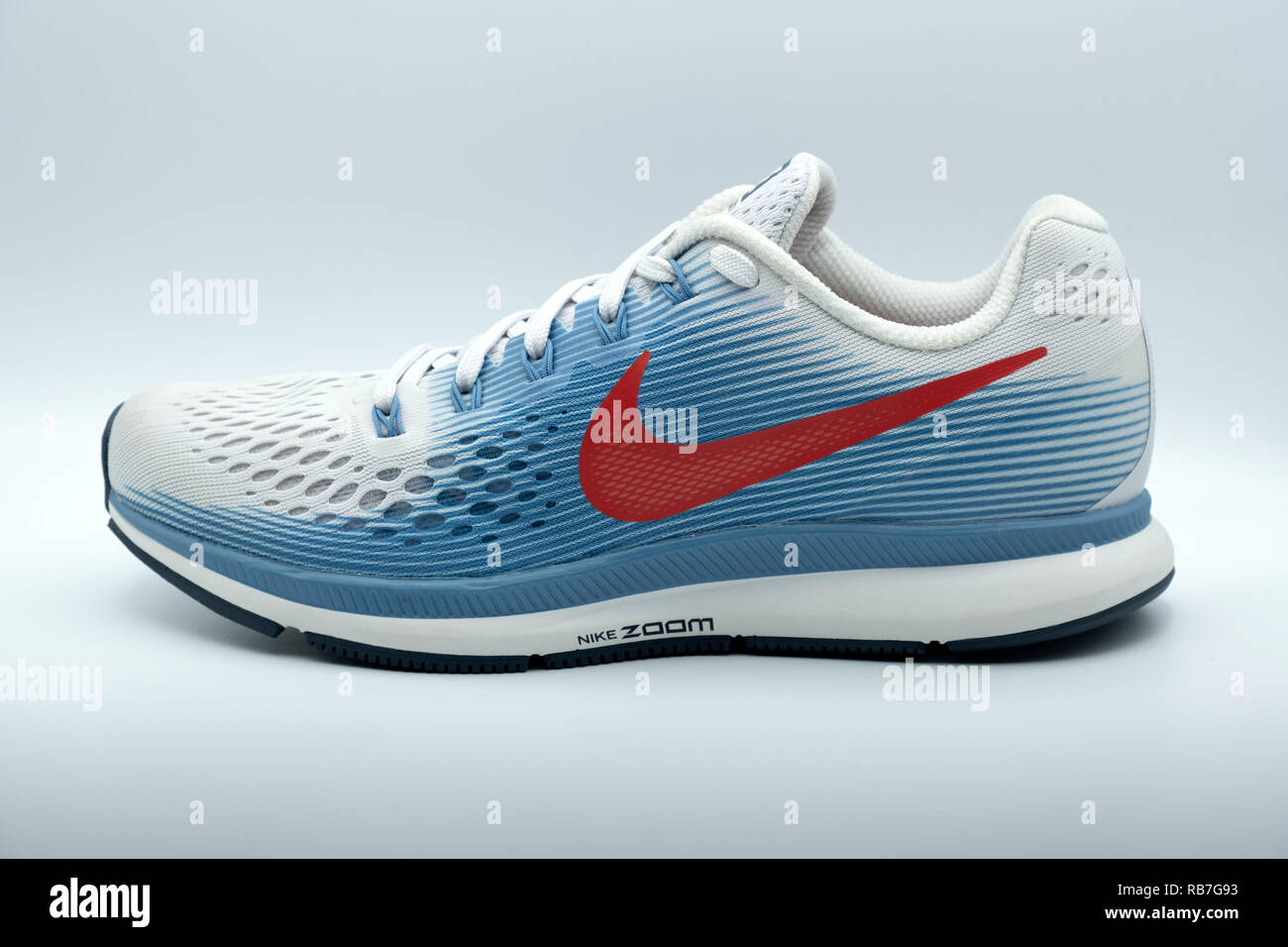 Lateral view of a blue and white Nike Pegasus 34 running shoe with a red swoosh logo cut out isolated on white background Stock Photo