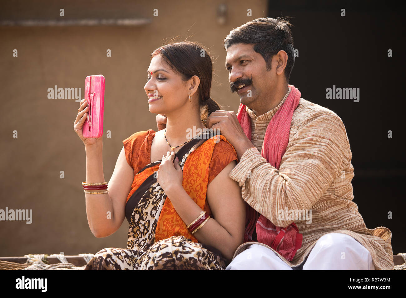 Rural Indian couple looking into mirror while sitting on traditional bed in village Stock Photo