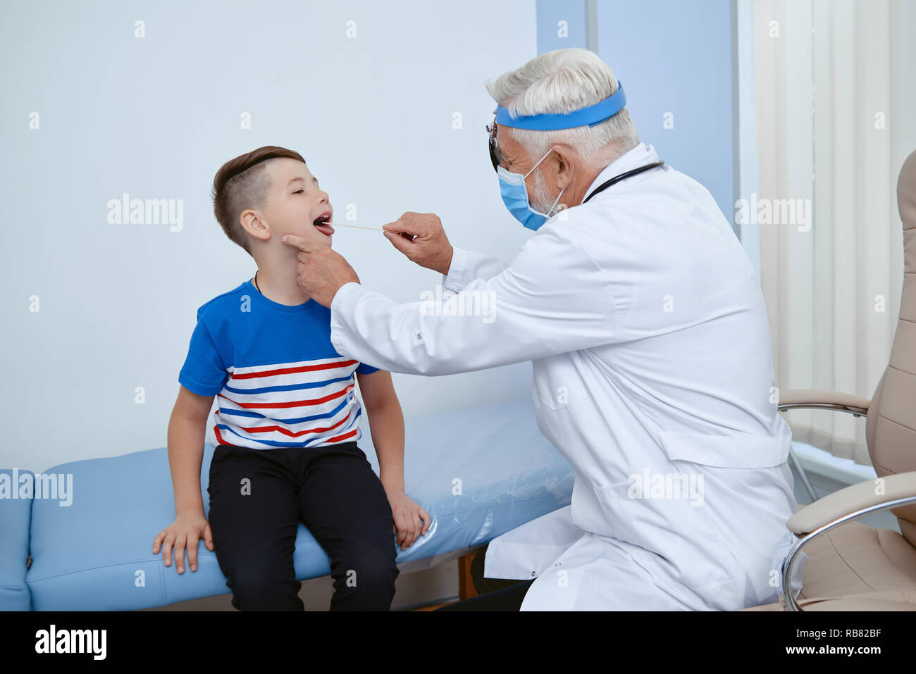 Portrait of doctor in uniform and mask working with little patient in hospital. Professional doctor helping providaing medical examination for ill boy. Concept of health care. Stock Photo