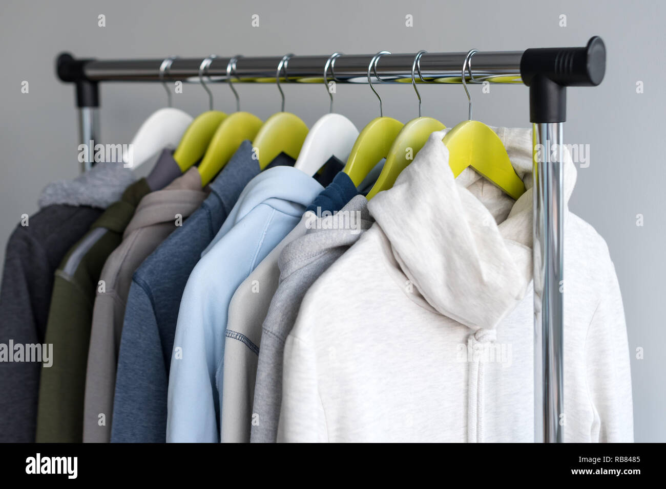 Hanger stand with spring or autumn warm clothes on grey background. Cold season, cozy sweaters and hoodie on hangers Stock Photo