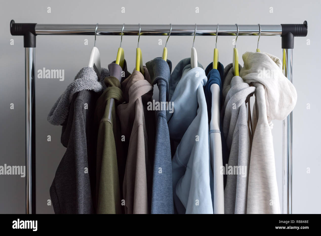 Hanger stand with spring or autumn warm clothes on grey background. Cold season, cozy sweaters and hoodie on hangers Stock Photo