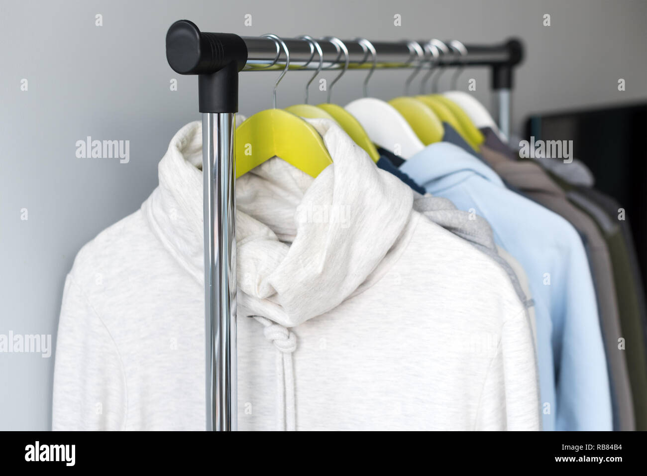 Hanger stand with spring or autumn warm clothes on grey background. Cold season, cozy sweaters and hoodie on hangers Stock Photo