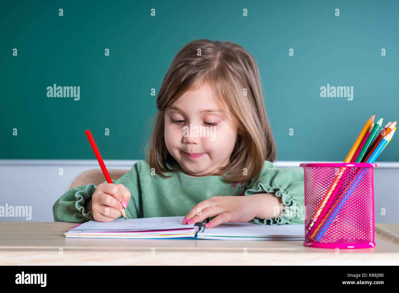 Little pretty girl sitting in the classroom at the gray desk and draws ...