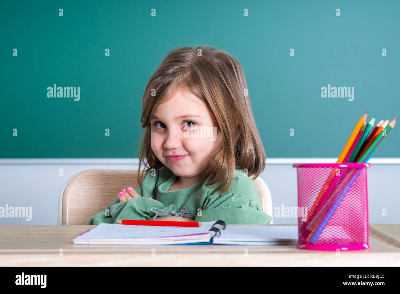 Little pretty girl sitting in the classroom at the gray desk and posing ...