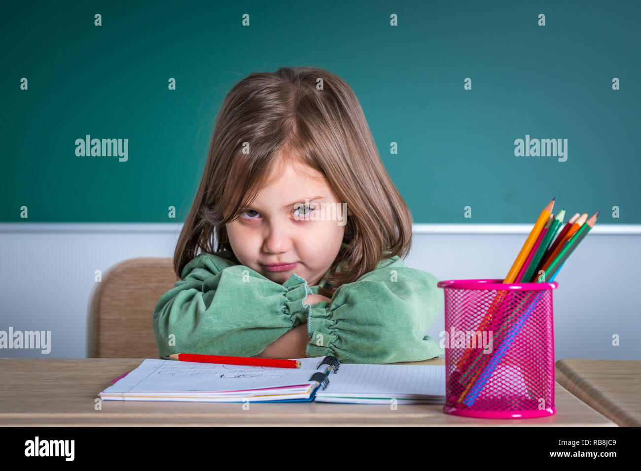 Little pretty girl sitting in the classroom at the gray desk and posing ...