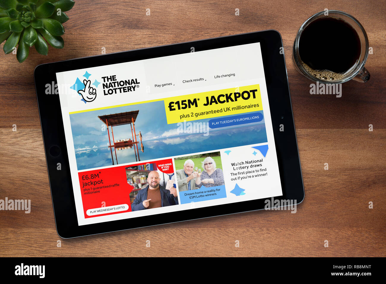 The website of The National Lottery is seen on an iPad tablet, on a wooden table along with an espresso coffee and a house plant (Editorial use only). Stock Photo