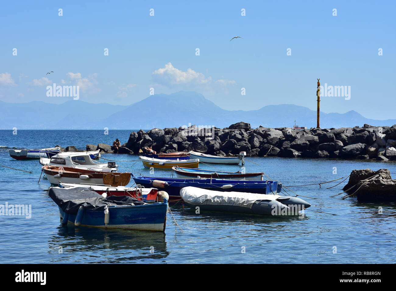 Small recreational and fishing boats moored in calm water behind artificial breakwall made of free laid stones on Mediterranean coast. Stock Photo