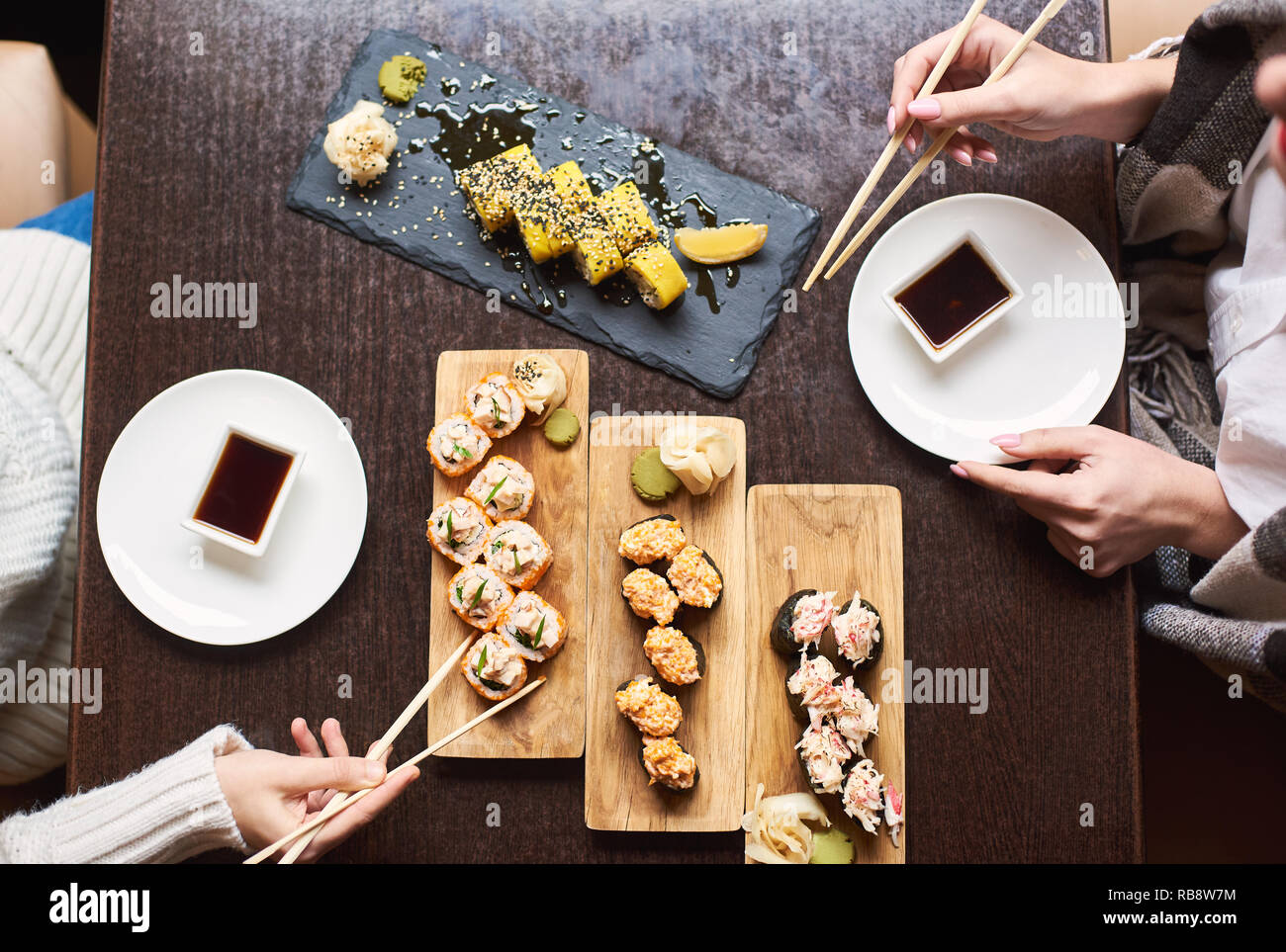 Friends coming to oriental restaurant for lunch. Women enjoying sushi set with soy sauce, wasabi