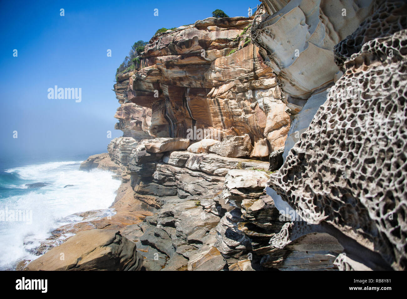 Dramatic rock formations eroded by wind and water near Bondi, Sydney, Australia. Colourful sandstone cliffs against blue sea/sky background Stock Photo