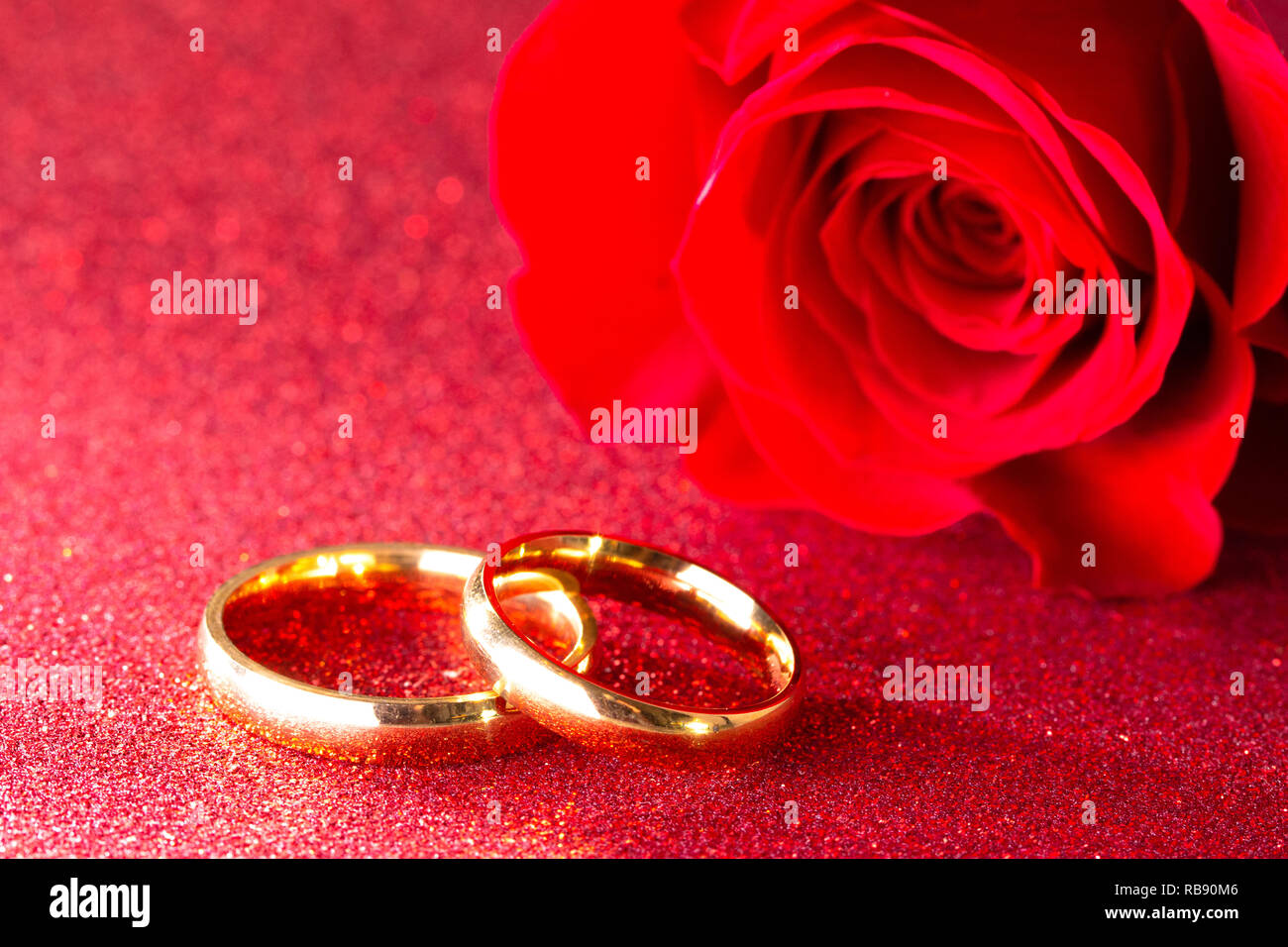 Gold Wedding Bands And A Red Rose On A Red Glitter Background Stock Photo Alamy