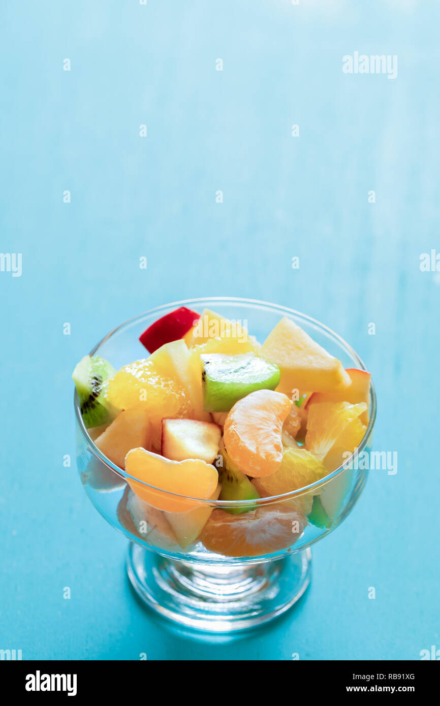 Fresh fruit salad in glass bowl on turquoise background with copy space ...