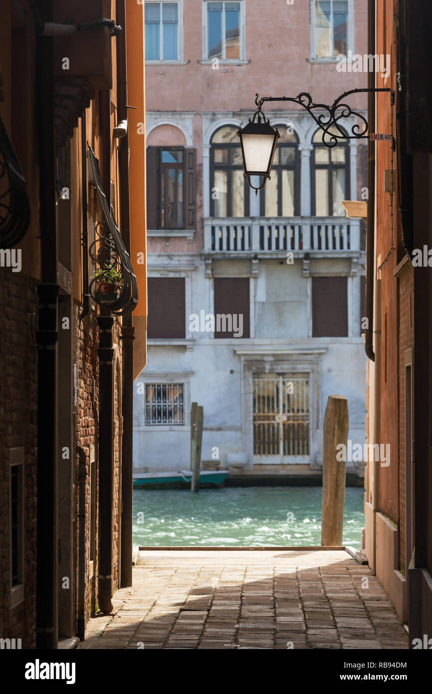 Narrow street with old lantern and view to the side canal in Venice, Italy Stock Photo
