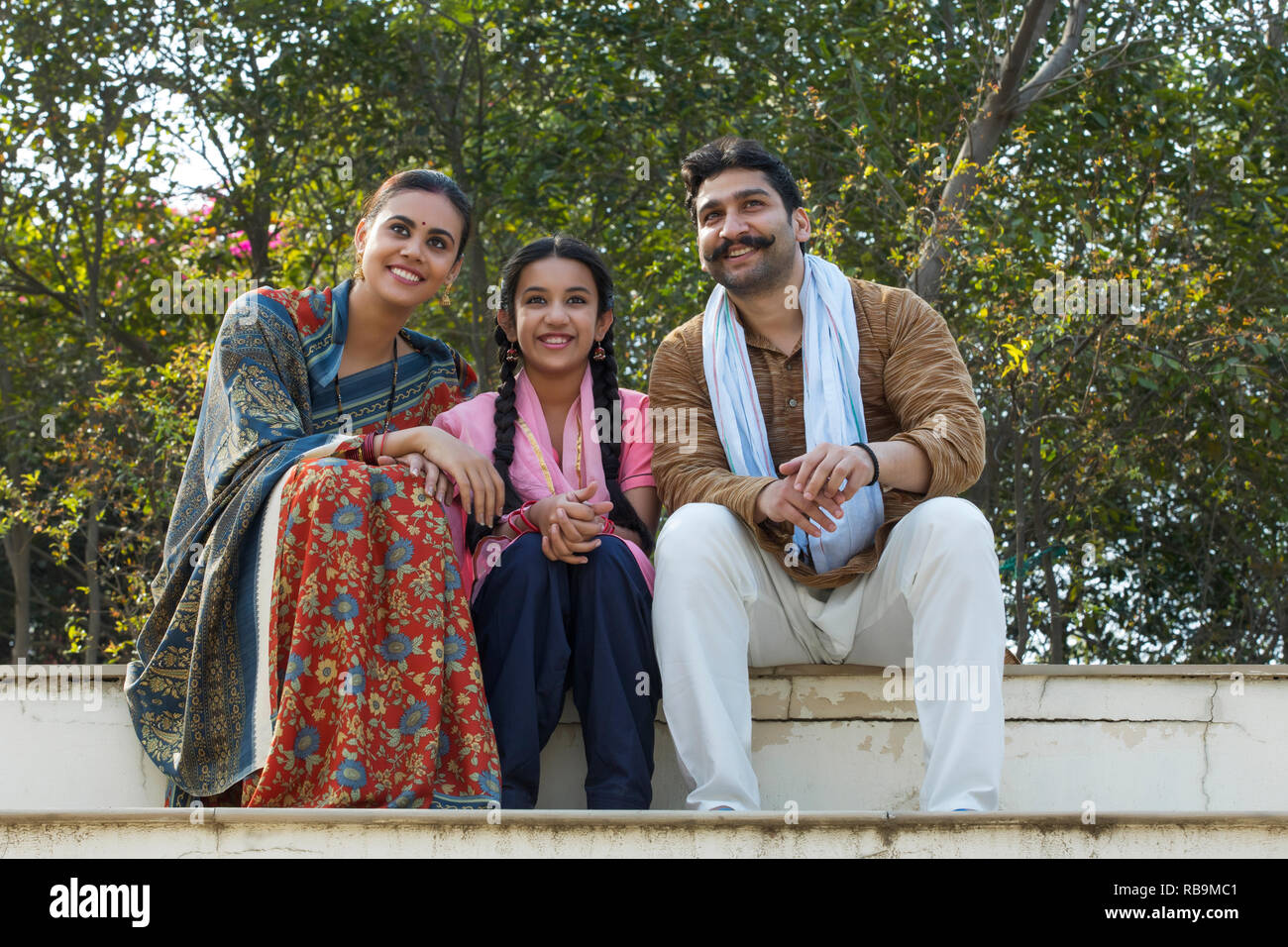 Happy village couple along with their young daughter sitting on steps ...