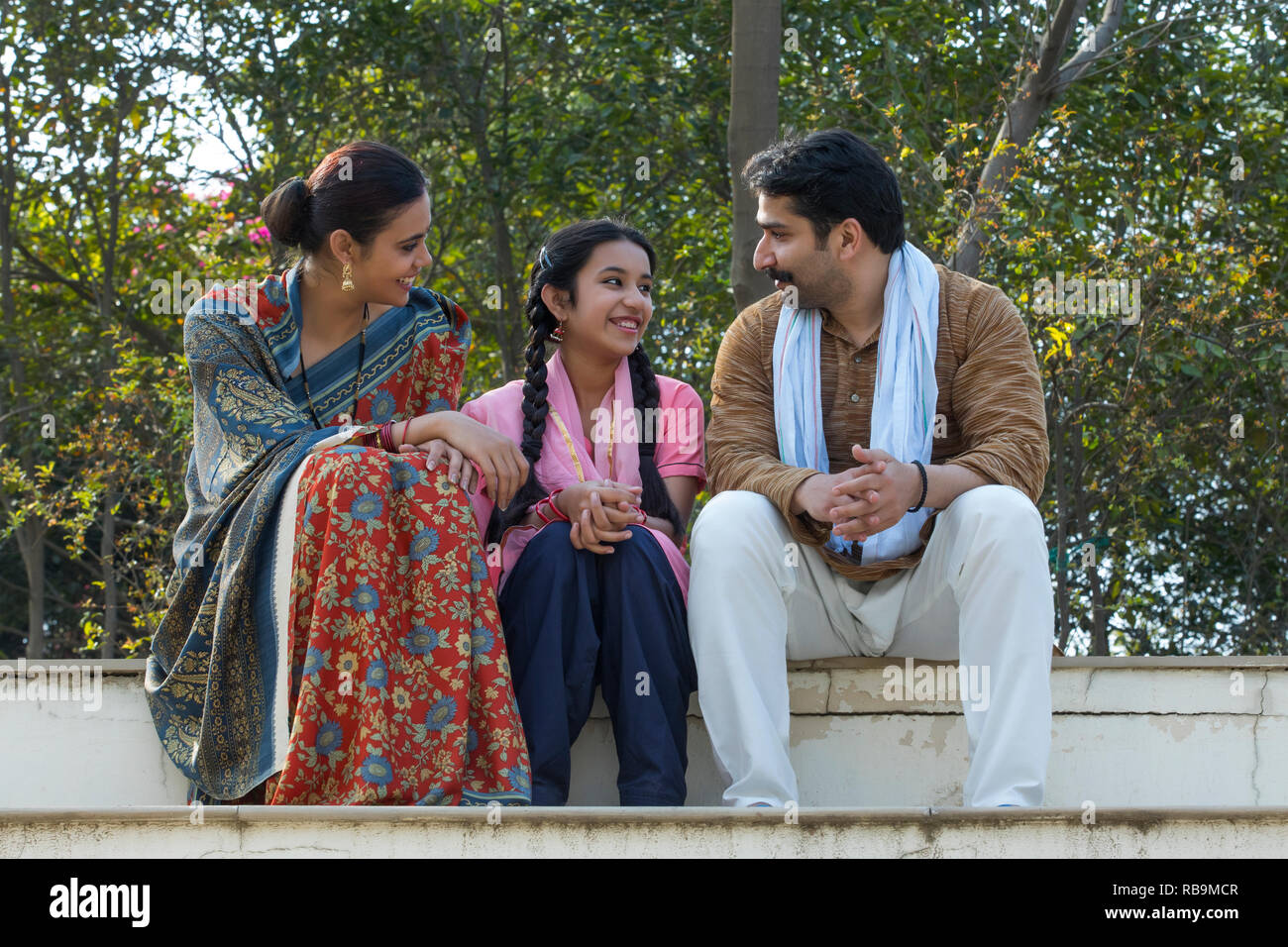 Happy village couple along with their young daughter sitting on steps ...