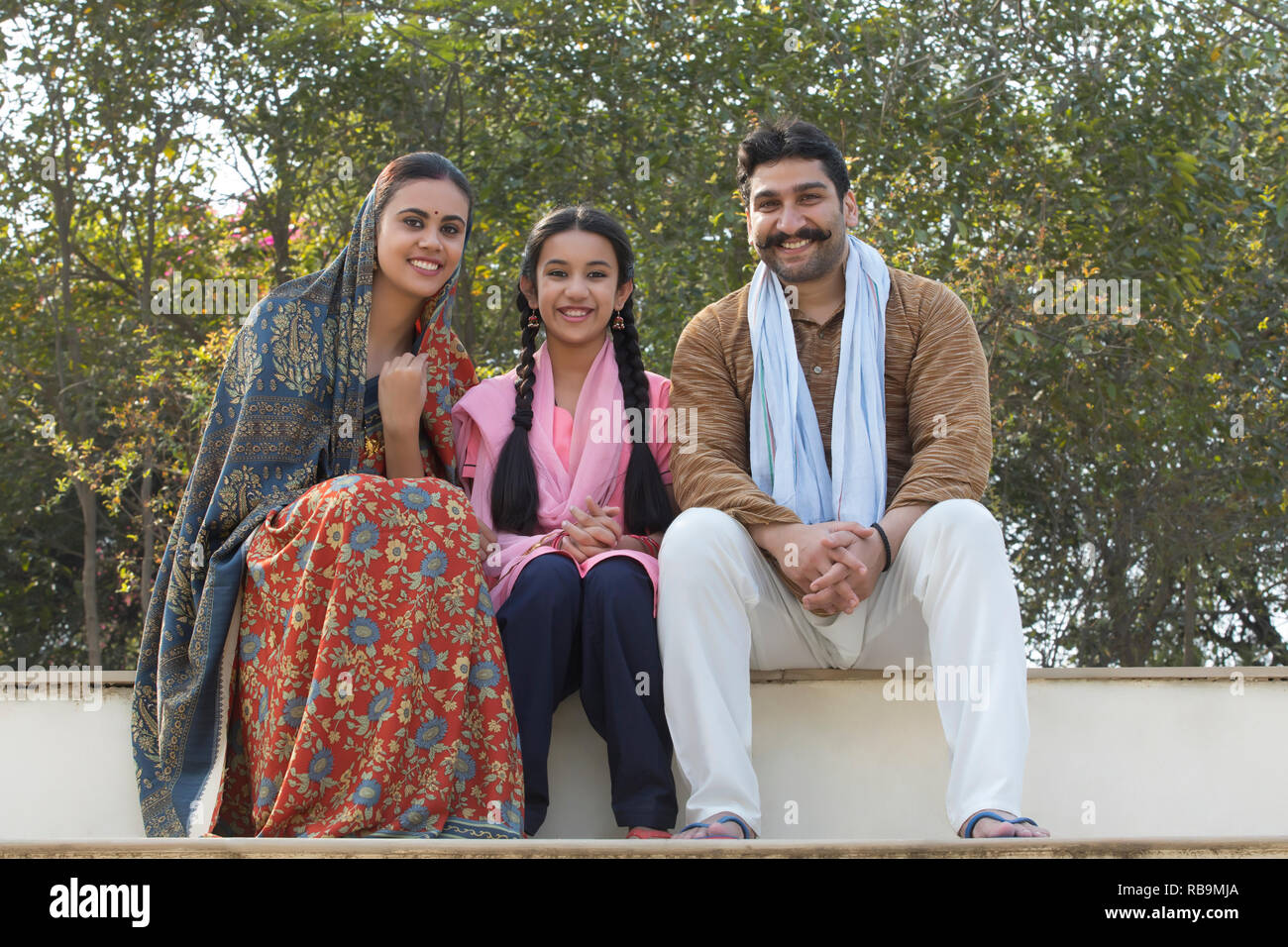 Happy village couple along with their young daughter sitting on steps ...