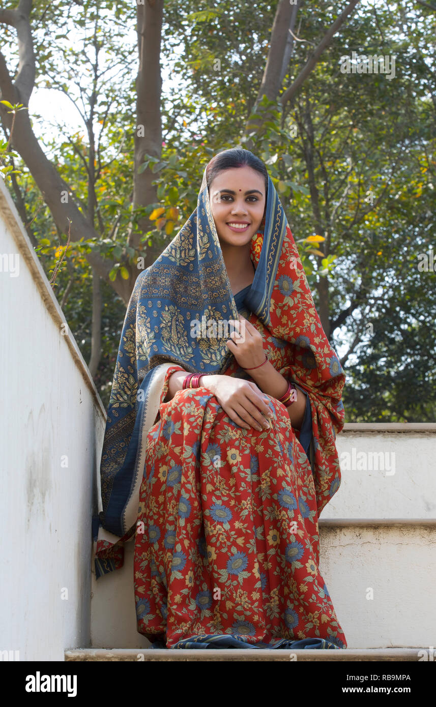 Smiling village woman sitting on the steps of her house leading to the terrace covering her head with saree. Stock Photo