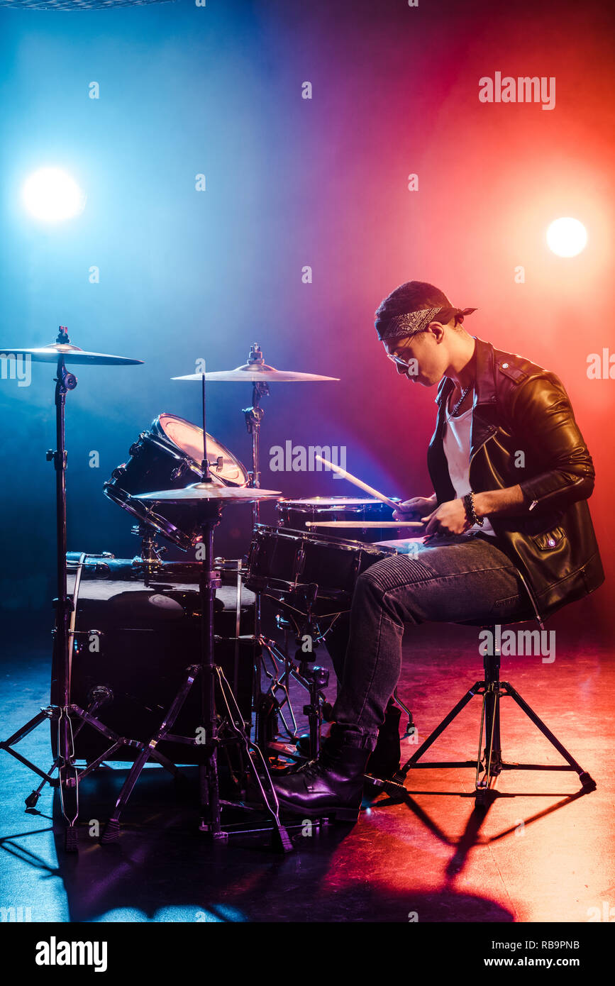 male rock star in leather jacket playing drums during concert on stage
