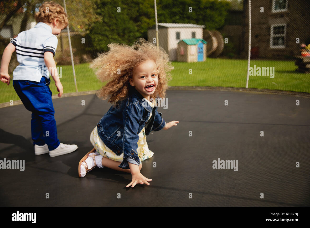 Little girl and boy playing on a tramploine outside. They are having fun and being playful. Stock Photo