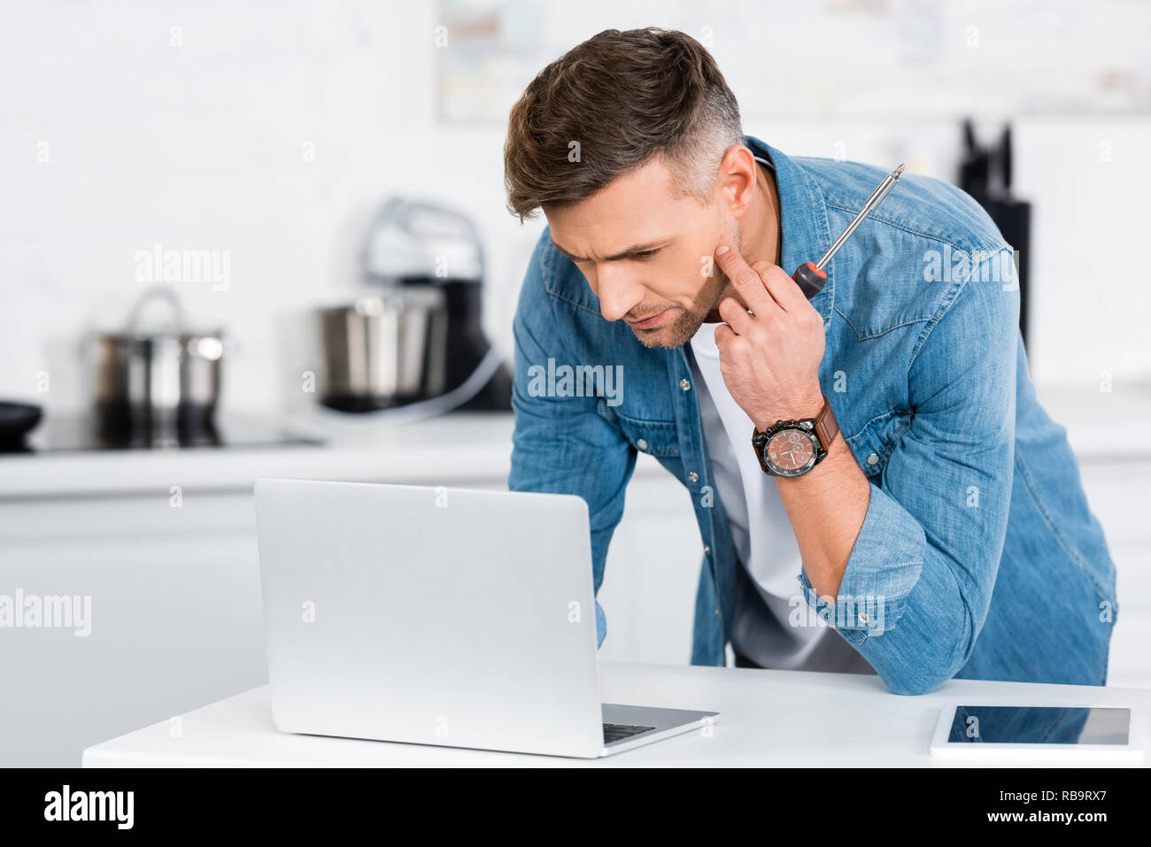 handsome man holding screwdriver and using laptop Stock Photo