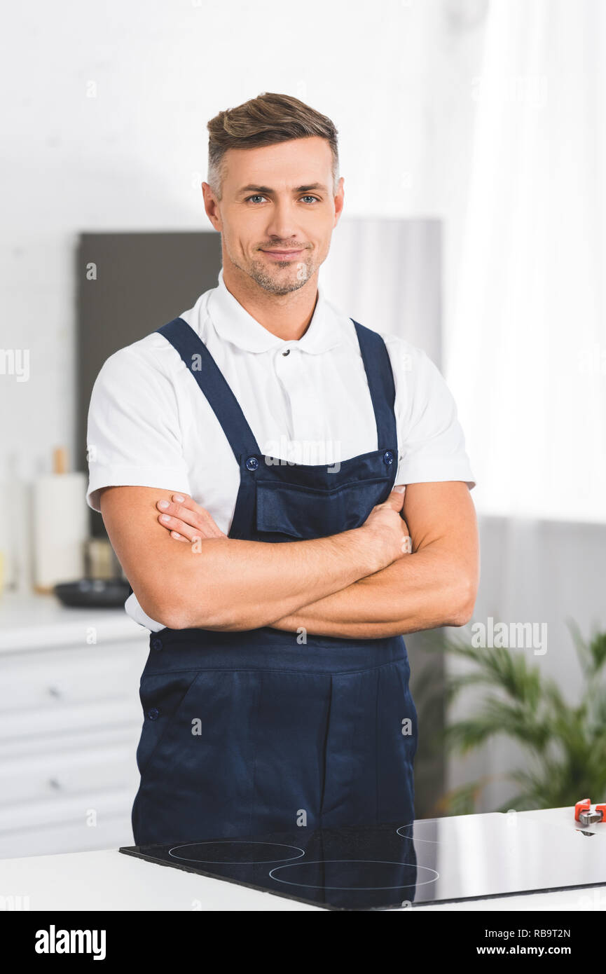 adult repairman standing near electric stove with crossed arms at