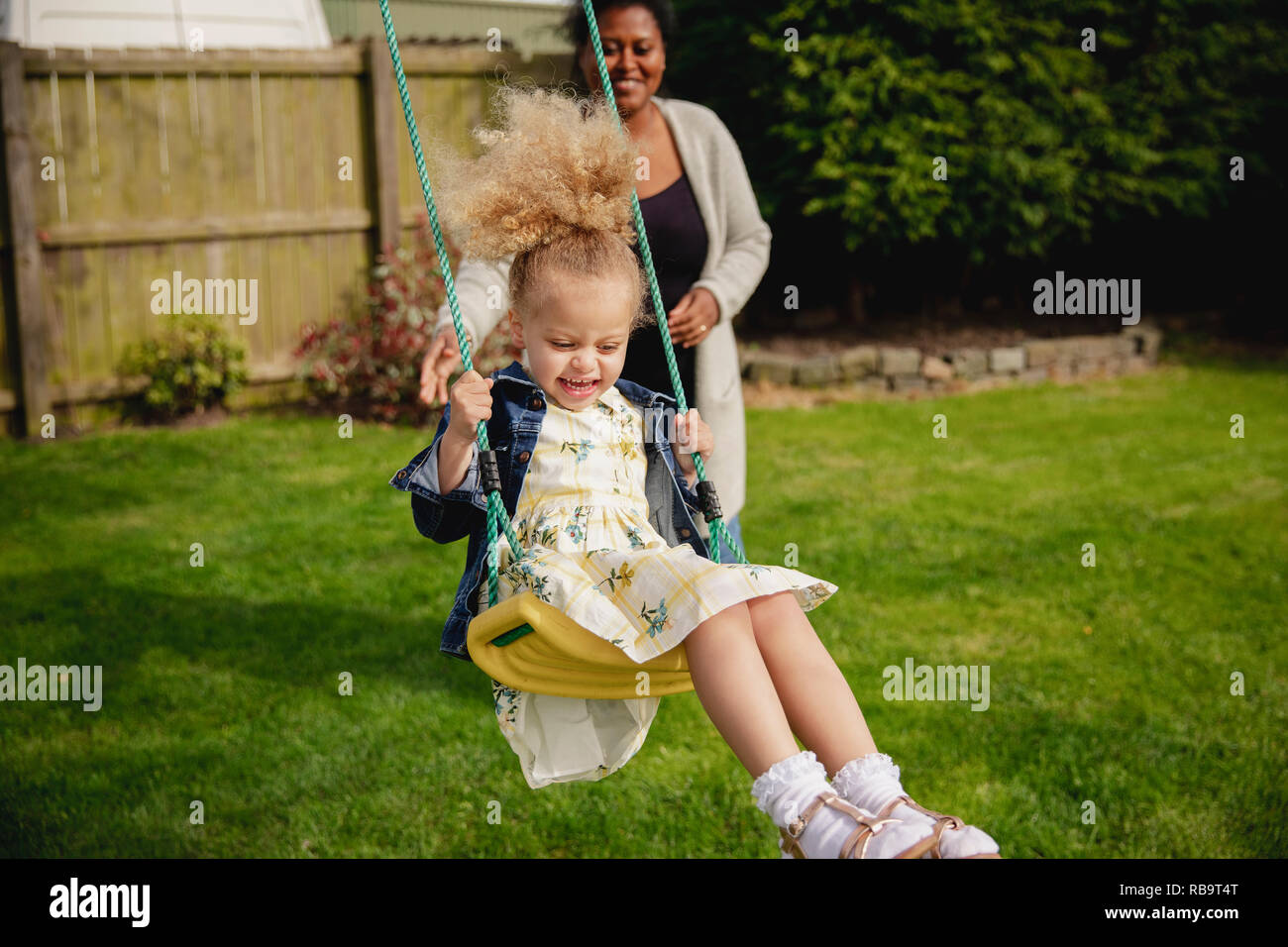 Little girl having fun while being pushed on a swing by her mother. Stock Photo