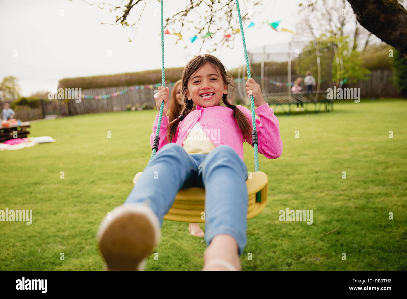 Little girl playing outside on a swing while her her mother helps and