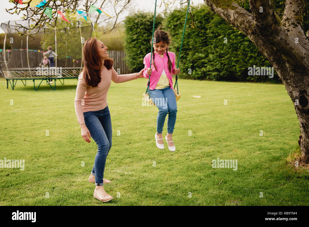 Little girl playing outside on a swing while her her mother helps and