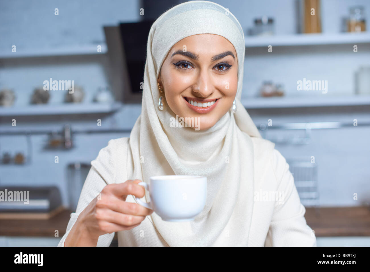 beautiful happy young muslim woman holding cup of coffee and smiling at camera Stock Photo