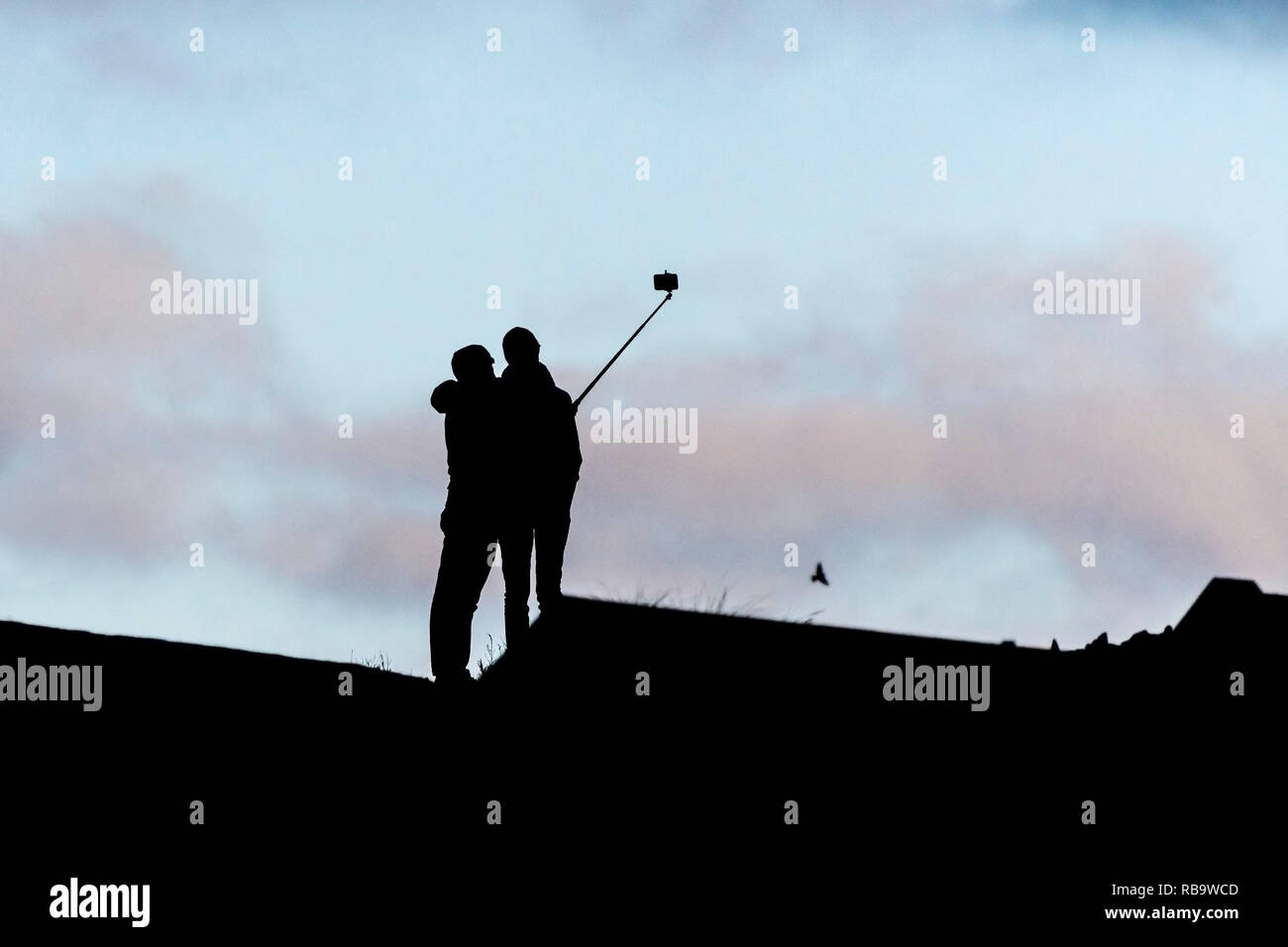 The silhouette of two people posing for a selfie photograph using a selfie stick. Stock Photo