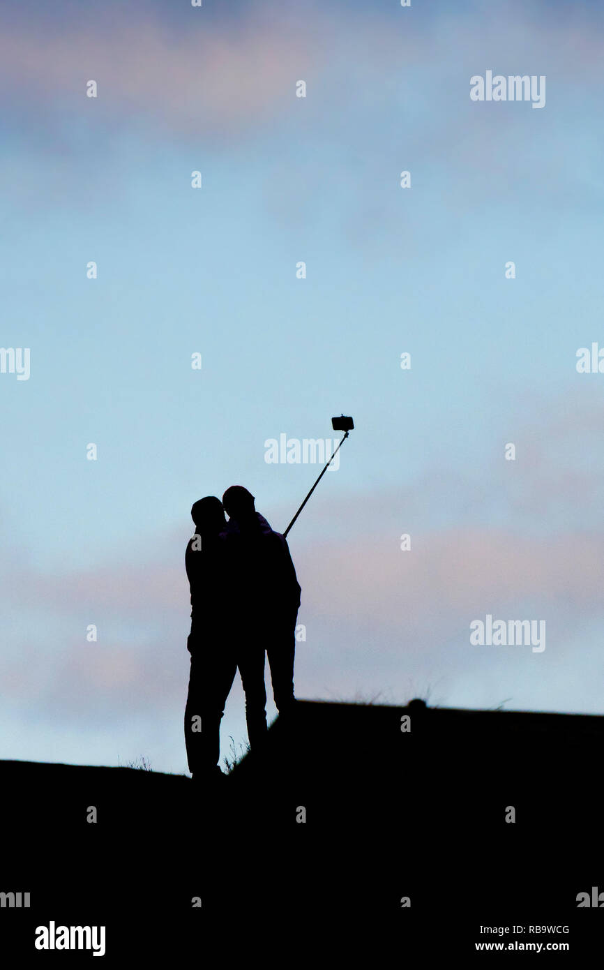 The silhouette of two people posing for a selfie photograph using a selfie stick. Stock Photo