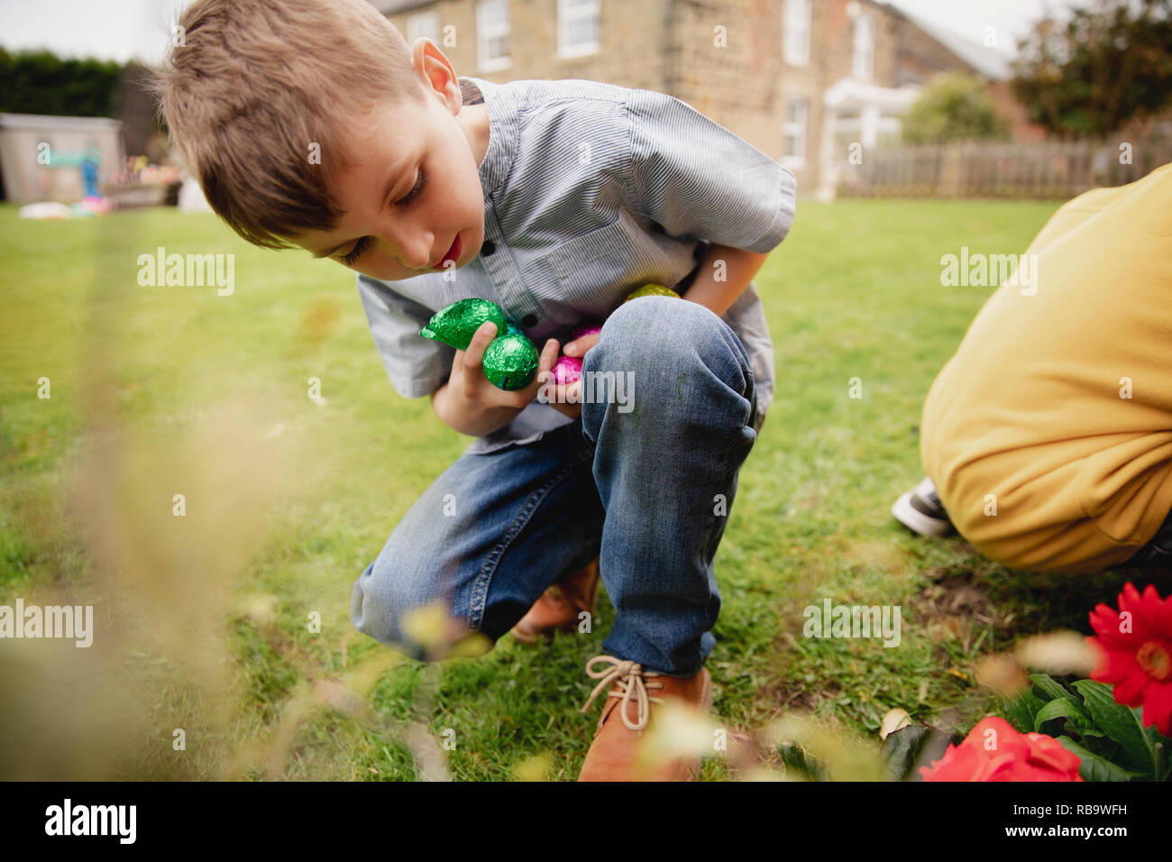 Young boy on an easter egg hunt with a friend. They are seaching for chocolate easter eggs in a back garden. Stock Photo